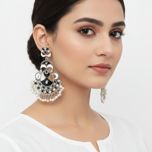 Ornate silver and black earrings with pearl-like beads on a dark background, featuring the brand 'Saheli'.