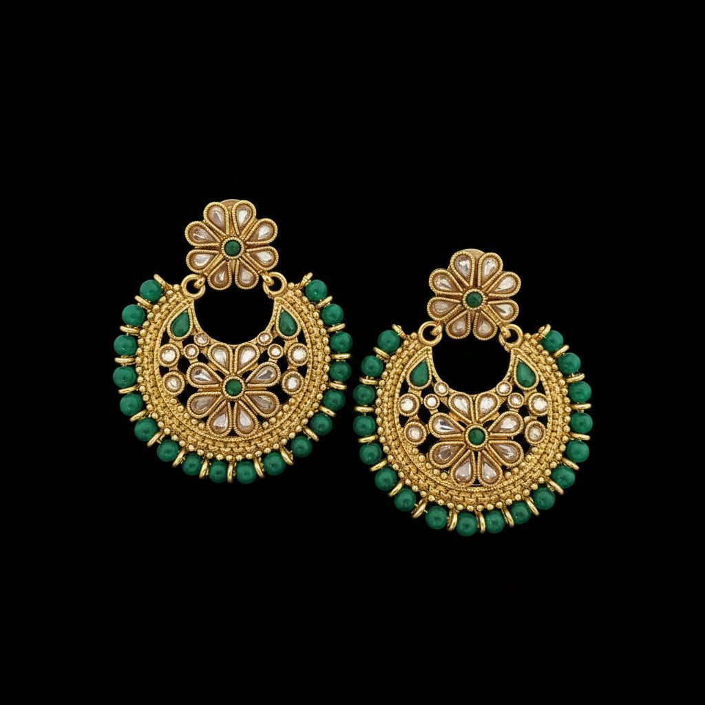 A pair of gold-toned Indian chandbali earrings decorated with green stones and white faux pearls, displayed on a dark reflective surface with the brand logo 'SAHELI MY BEST FRIEND' at the top.