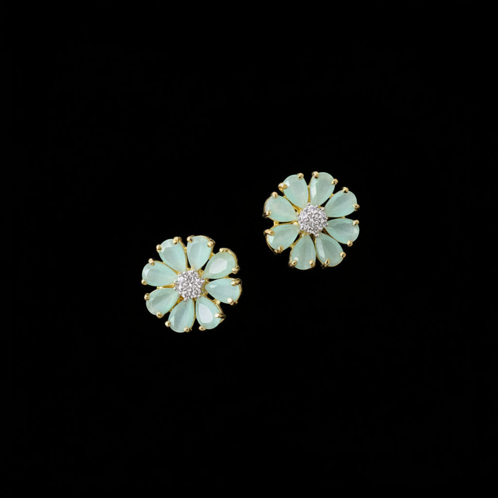 Pair of light blue flower-shaped earrings with gold accents on a gray surface.