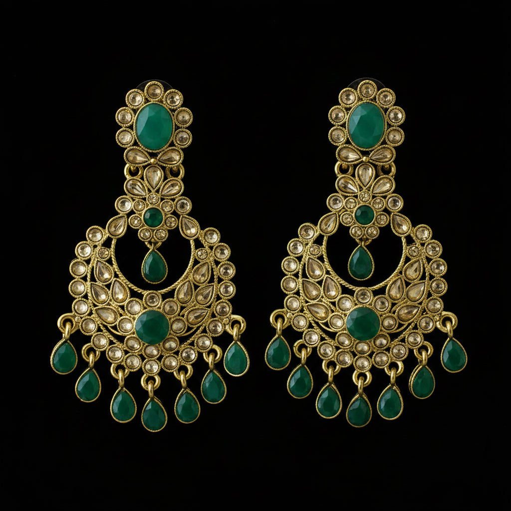 A pair of gold-plated Indian jhumka earrings with green stone accents and small white bead details, displayed on a dark reflective surface. The brand logo 'SAHELI MY ELLIE FRIEND' is visible in the top left corner.