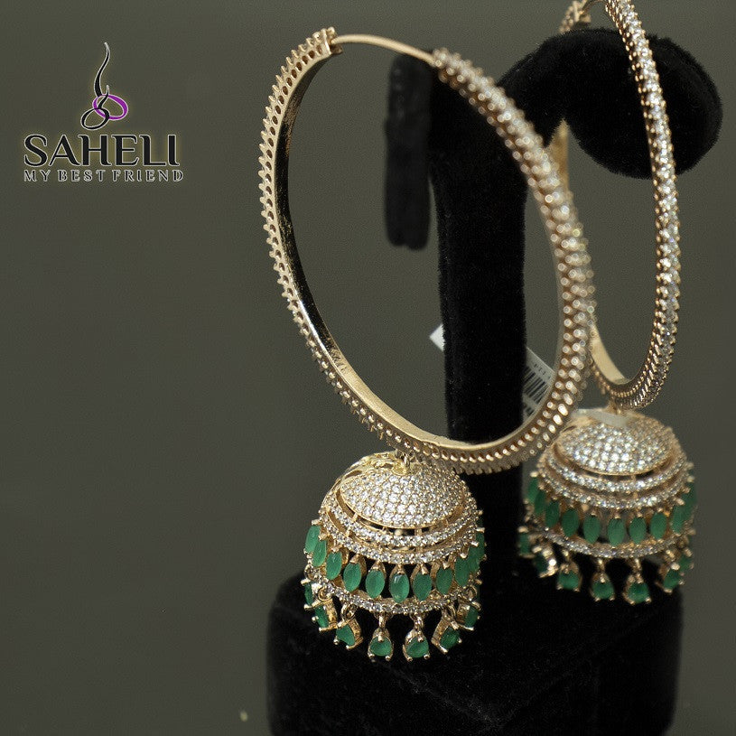 Gold hoop earrings with green gemstones on a black stand, branded 'Saheli'.