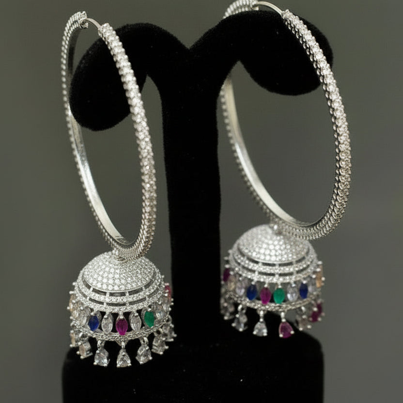 Gold hoop earrings with intricate designs and colorful gemstones on a black stand, branded 'Saheli'.