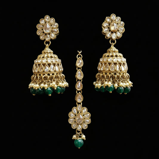 Gold and green earrings on a gray stand with 'Saheli' branding.
