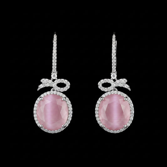 A pair of silver drop earrings with oval pink gemstones and small clear stones, displayed on a textured brown wood background.