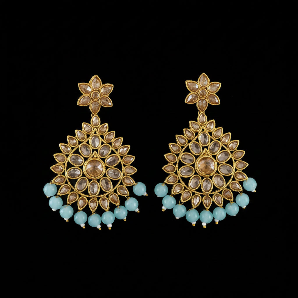 A pair of gold-toned Indian jhumka earrings with clear stones and light blue bead accents, displayed on a dark gray background with a 'SAHELI MY BEST FRIEND' watermark.