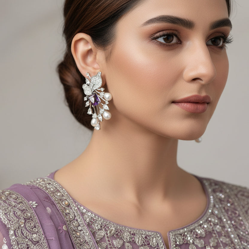 Pair of silver earrings with pearls and purple stones on a gray cushion