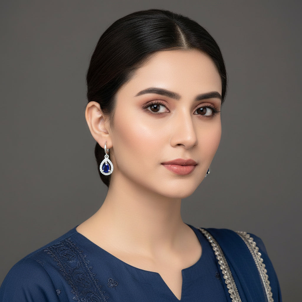 Pair of silver earrings with blue stones on a dark background, branded 'Saheli'.