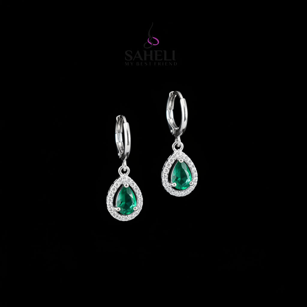 Silver earrings with green gemstones on a dark background, featuring the brand 'Saheli'.