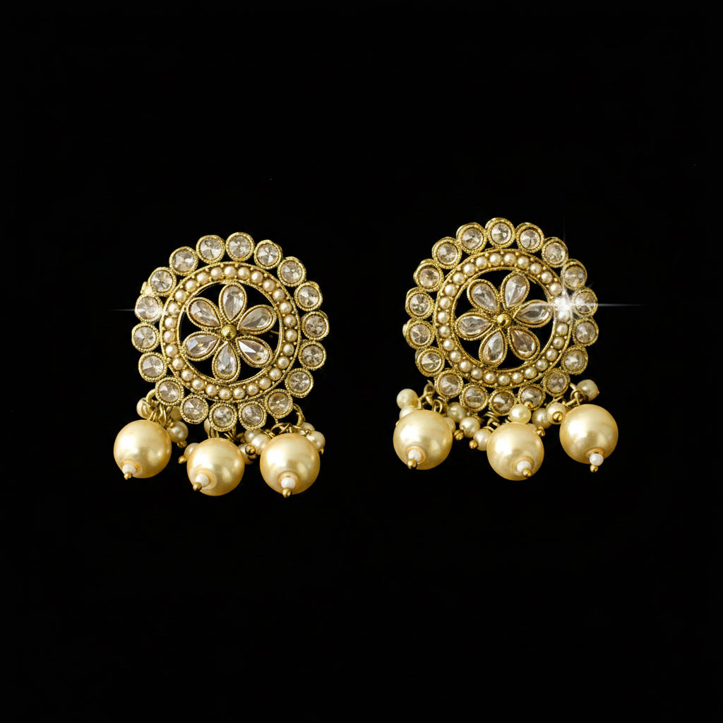 Pair of gold earrings with floral designs and pearl-like beads on a dark background