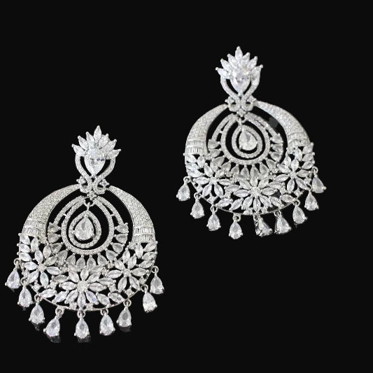 Pair of silver earrings with intricate designs on a dark background, featuring the brand 'Saheli'.