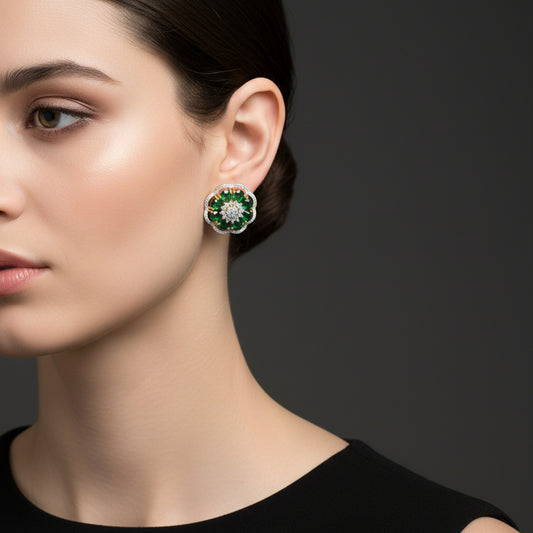 Pair of floral earrings with green gemstones and gold accents on a gray surface.