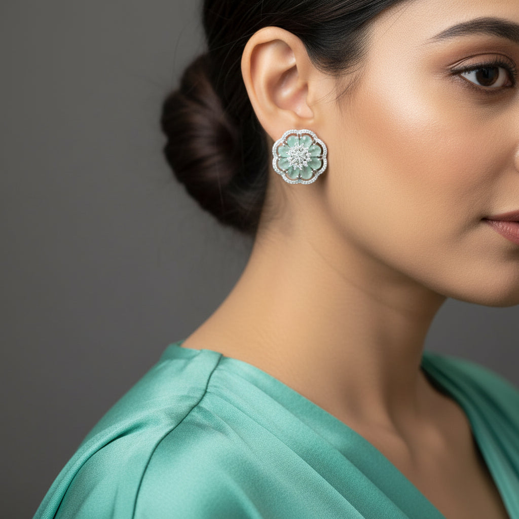 Pair of flower-shaped earrings with green gemstones and silver accents on a gray surface.
