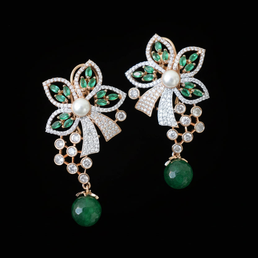Pair of decorative earrings with green gemstones and pearl on a gray cushion