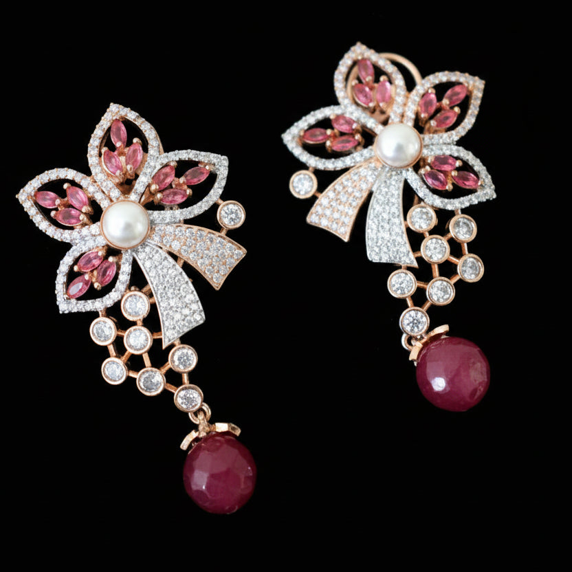 Pair of ornate earrings with pink gemstones and pearl-like centers on a gray surface.