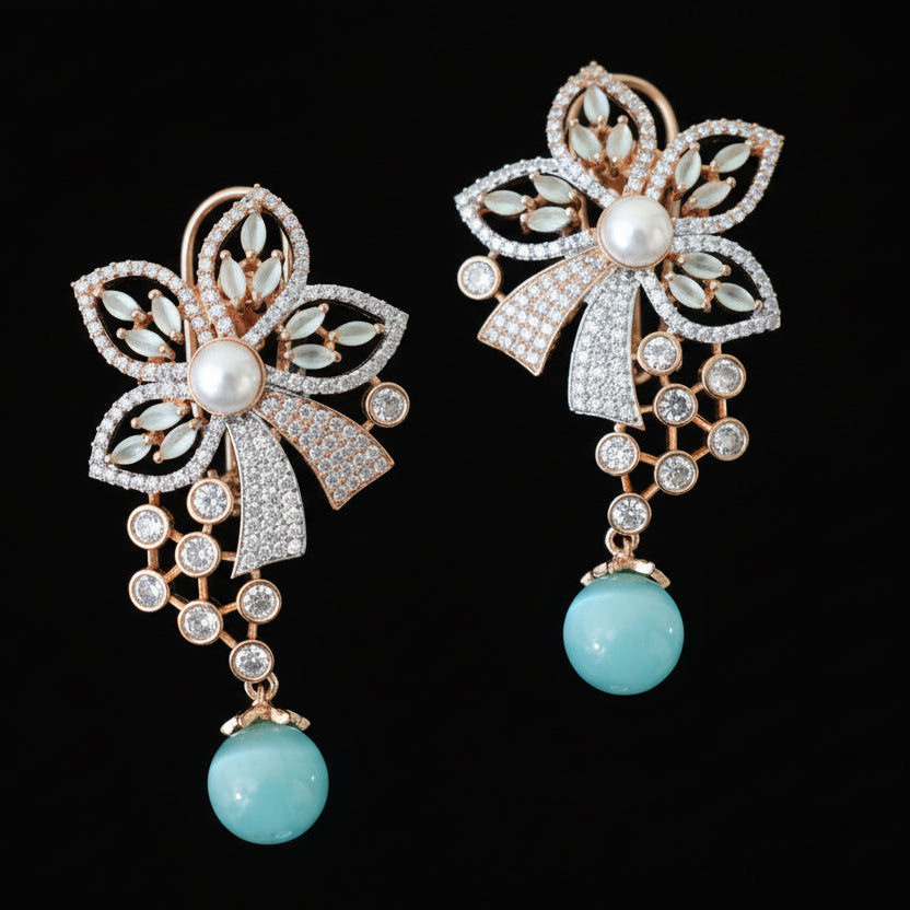 Pair of decorative earrings with floral designs and turquoise beads on a gray surface.