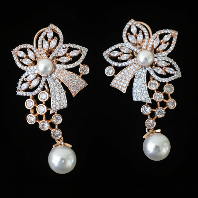 Pair of decorative earrings with floral designs and pearl drops on a gray surface.