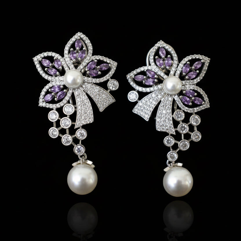 Pair of decorative earrings with purple gemstones and pearls on a gray surface