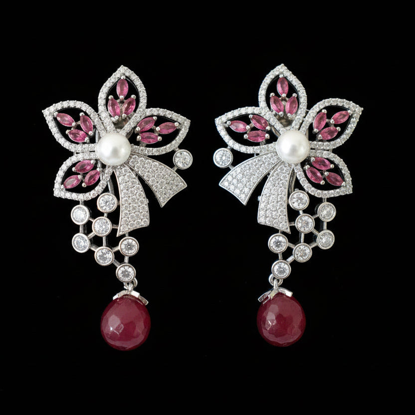 Pair of earrings with pink gemstones and red beads on a gray surface