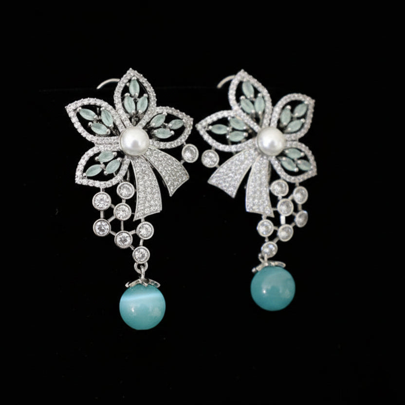 Pair of floral earrings with turquoise beads on a gray cushion