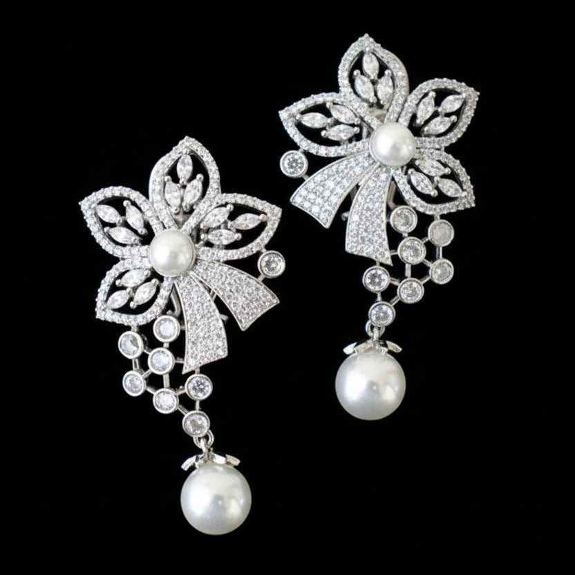 Pair of silver floral earrings with pearl drops on a gray cushion.