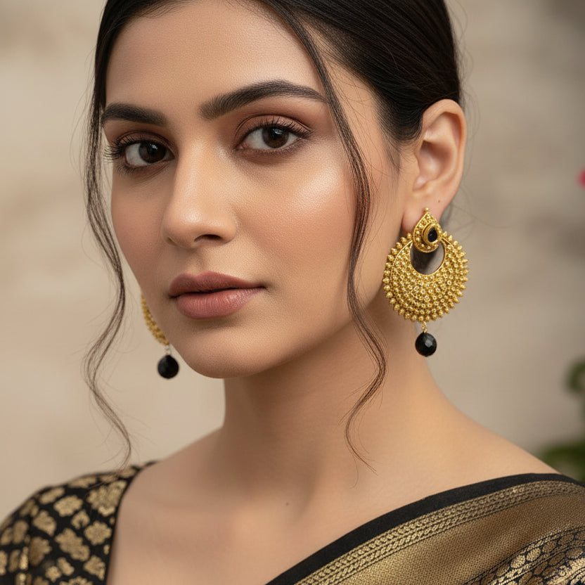 Pair of gold earrings with black beads on a gray background