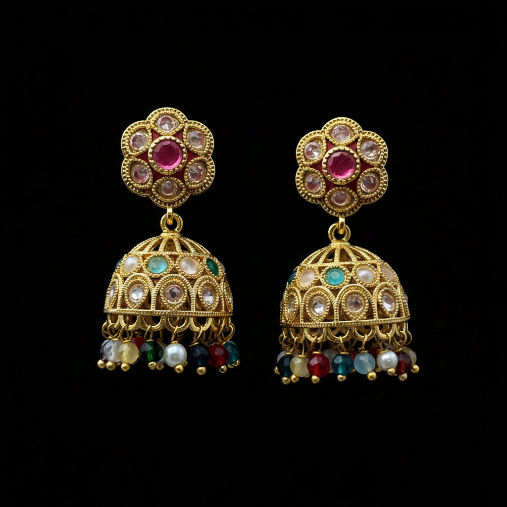A pair of gold-plated Indian jhumka earrings with multicolor stones and dangling beads, displayed on a solid dark pink background.