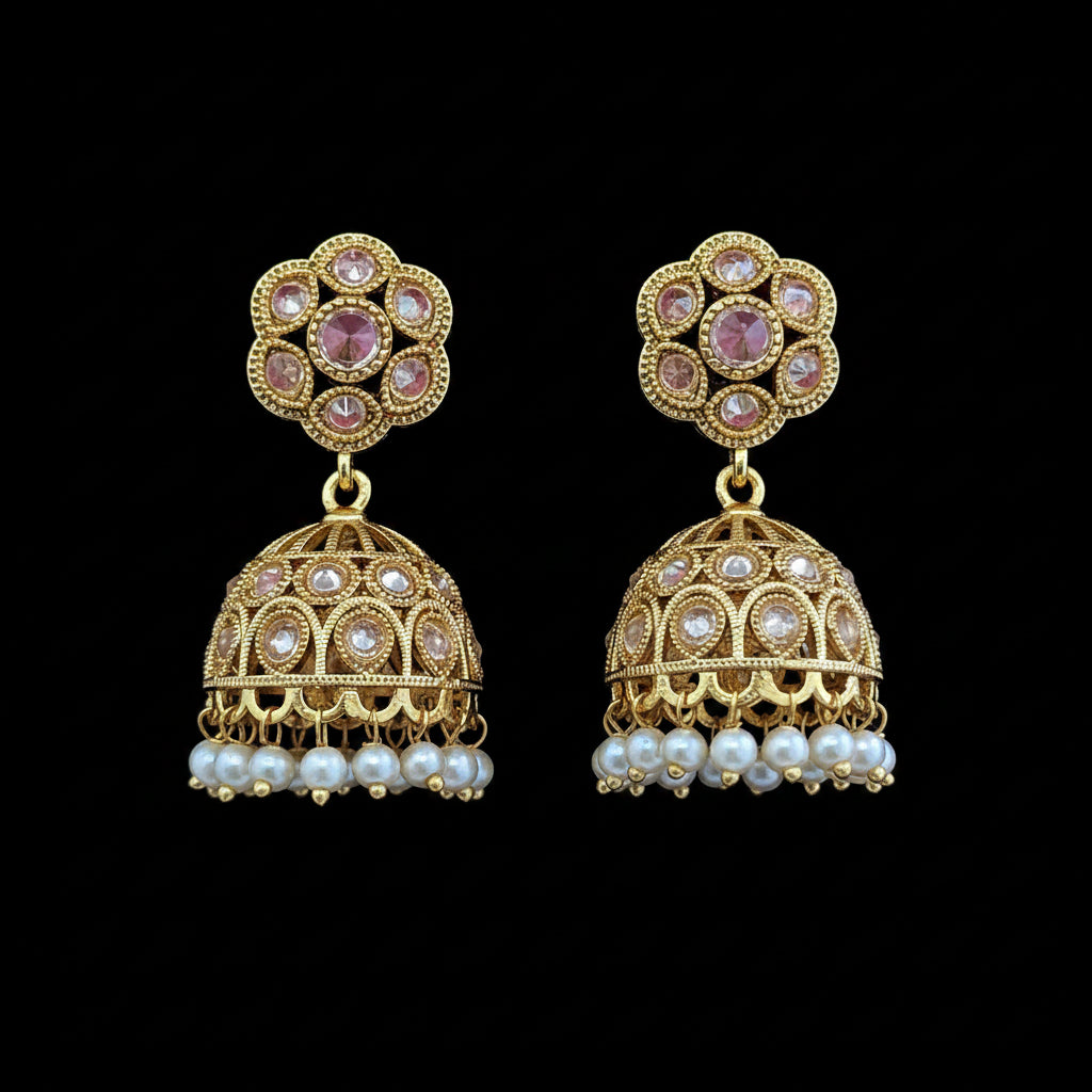 A pair of gold-toned Indian jhumka earrings with pink stones and white pearls, displayed on a solid dark pink background.