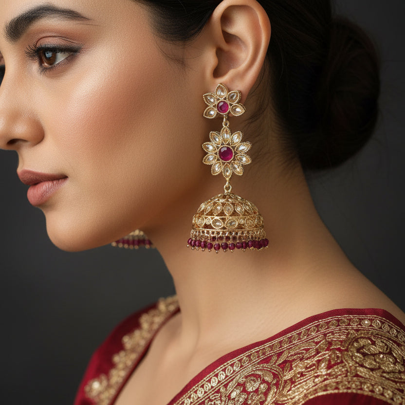 Gold and red gemstone earrings on a dark stand with 'SAHELI' branding.