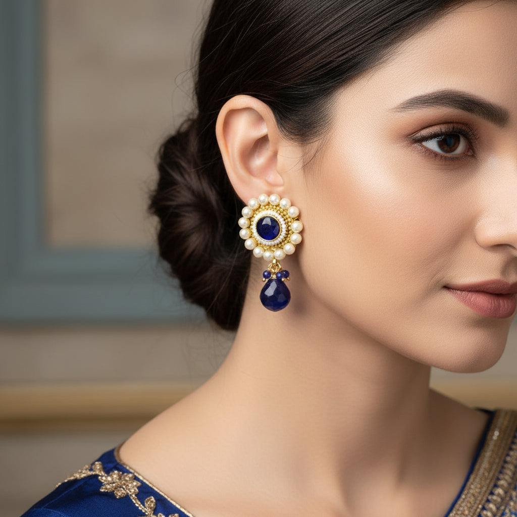 Pair of earrings with pearls and blue stones on a gray background, featuring the brand 'Saheli'.