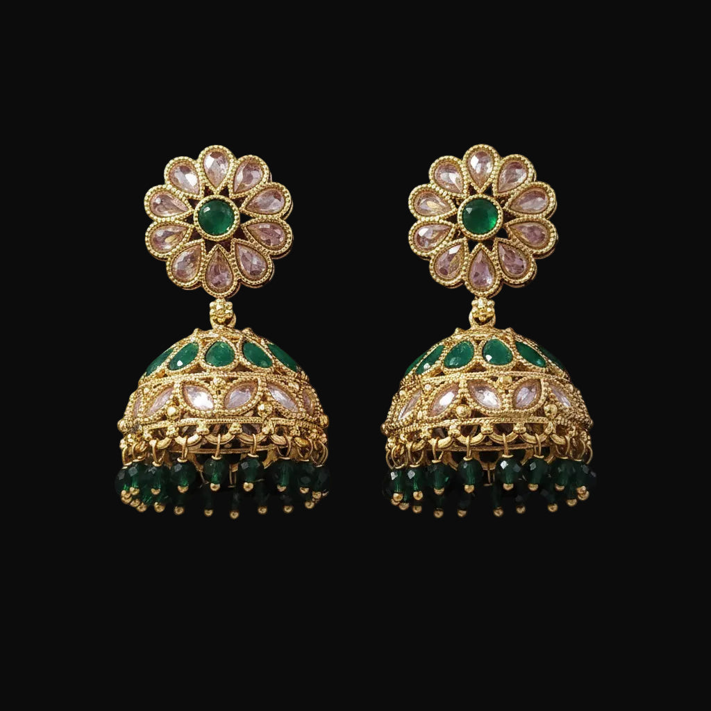 A pair of gold-plated Indian jhumka earrings with green and light pink stones, displayed on a solid dark pink background.