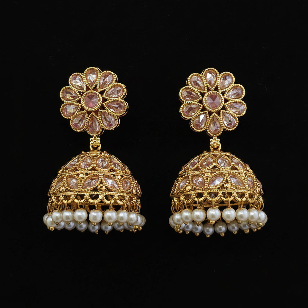 A pair of ornate gold jhumka earrings with pink gemstone floral studs and dangling pearl rows, displayed on a solid dark red background.