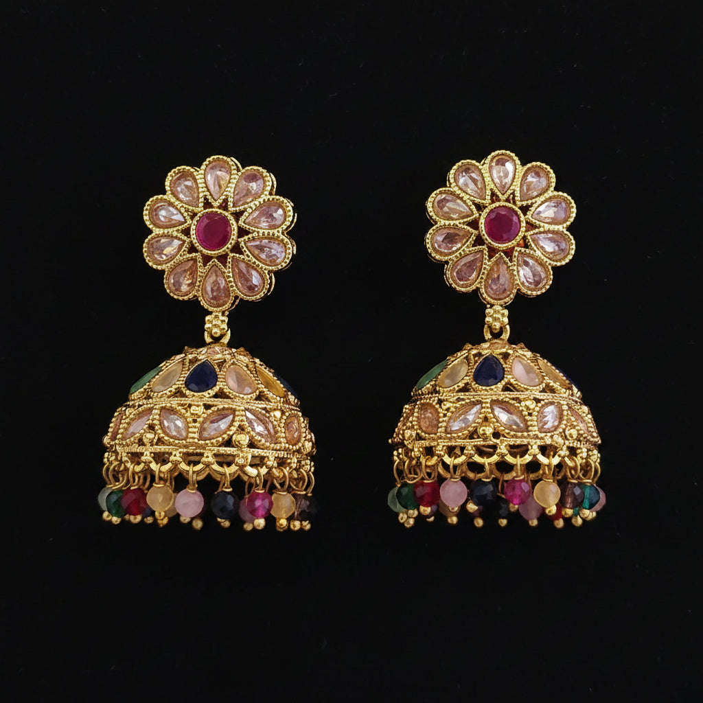 A pair of ornate gold-plated Indian jhumka earrings decorated with pink, blue, and multicolor stones, displayed on a solid dark pink background.