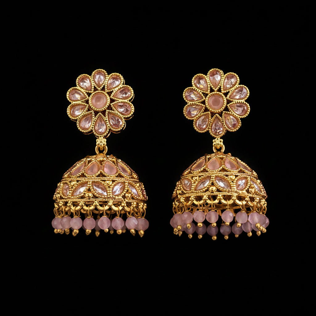 A pair of ornate gold-toned jhumka earrings with pink stone accents and dangling bead chains, displayed on a solid red background.