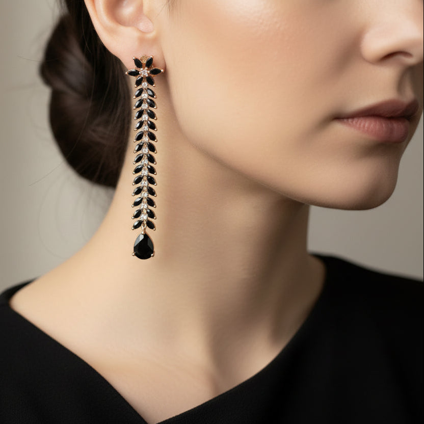 Pair of long, thin earrings with star-like tops on a dark gray background