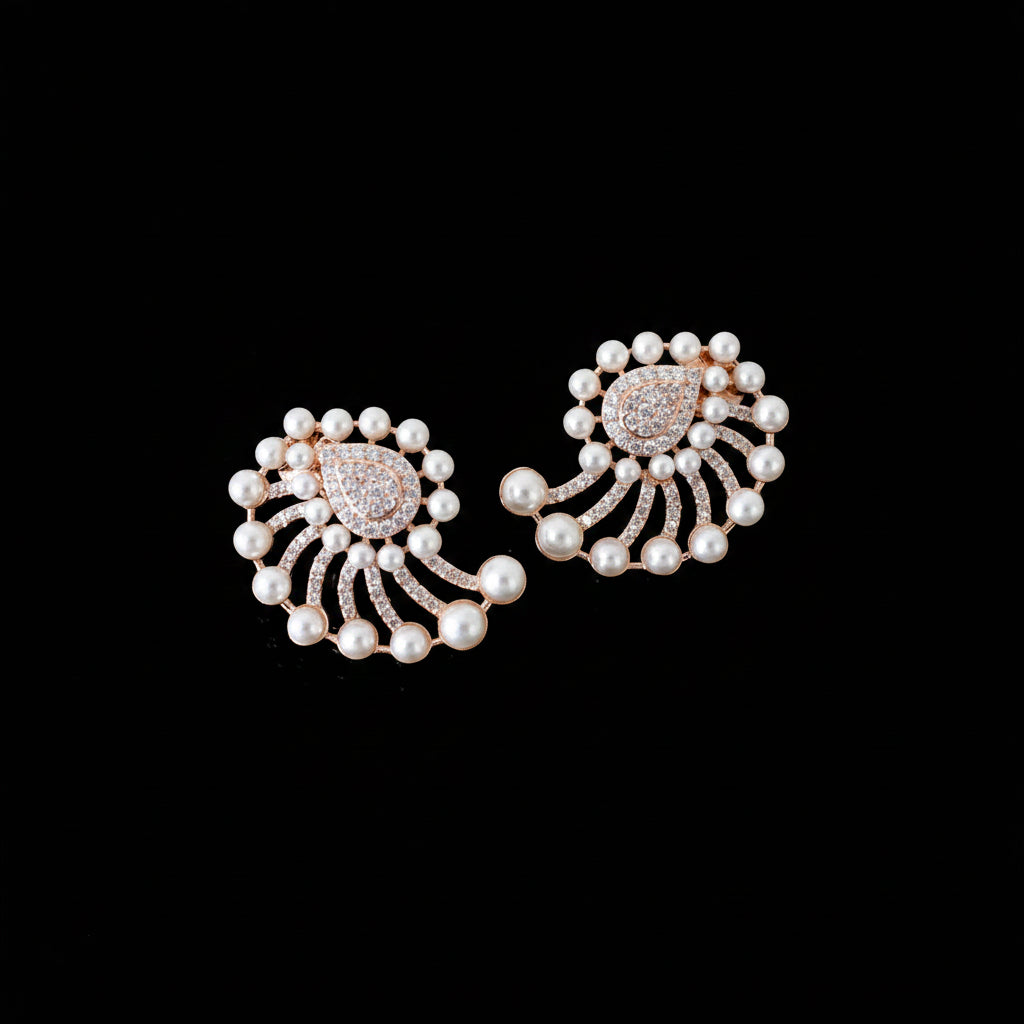 A pair of ornate pearl and rose gold earrings with a floral or fan-like design, displayed on a dark reflective surface.