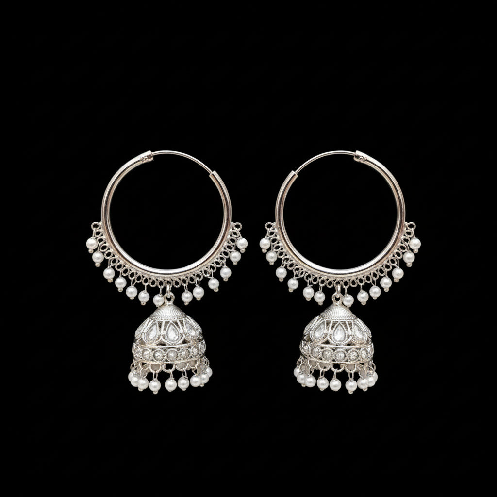 Silver hoop earrings with pearl drops on a black stand, branded 'Saheli'.