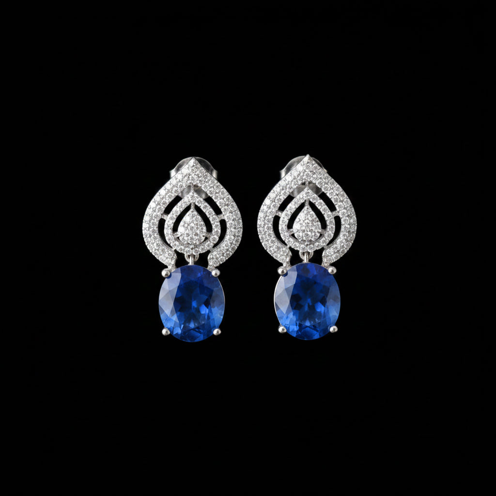 Pair of silver earrings with blue stones on a gray background, branded 'Saheli'.