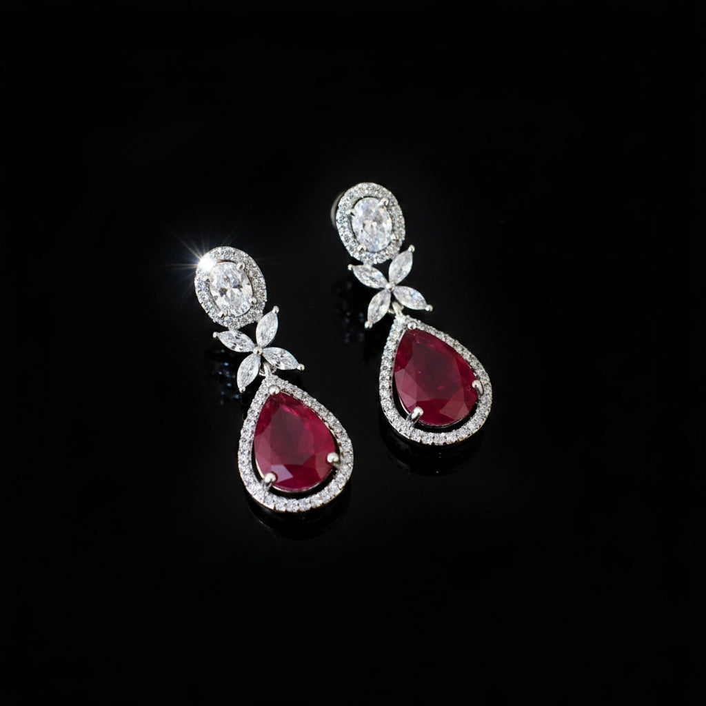 Pair of teardrop-shaped earrings with red gemstones and silver accents on a dark background