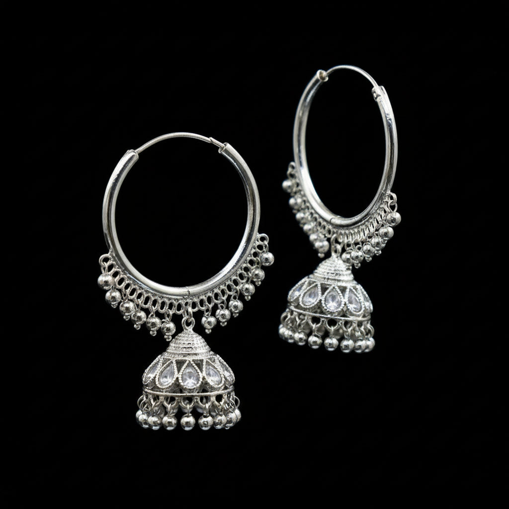 Silver hoop earrings with Jhumka designs on a black stand against a dark background.