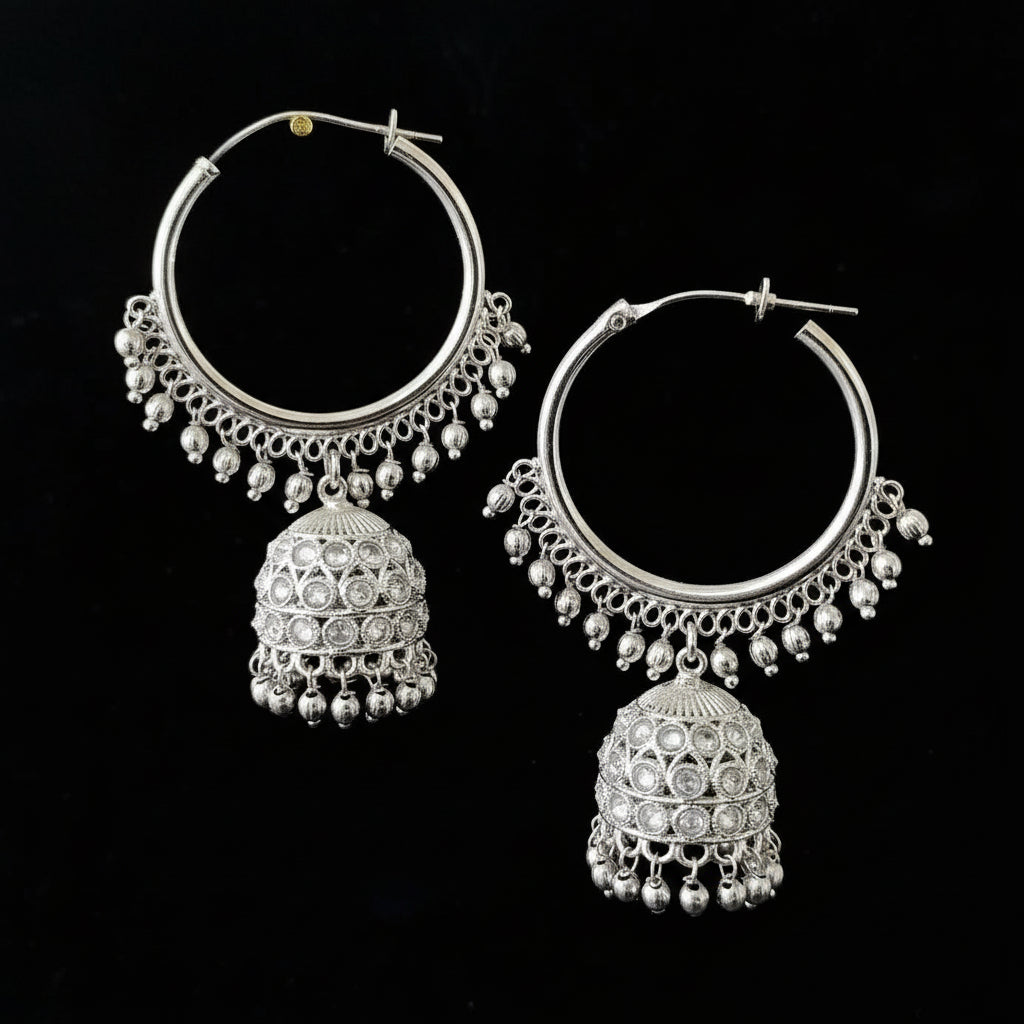 Silver hoop earrings with jhumka designs on a black background, featuring the brand 'Saheli'.