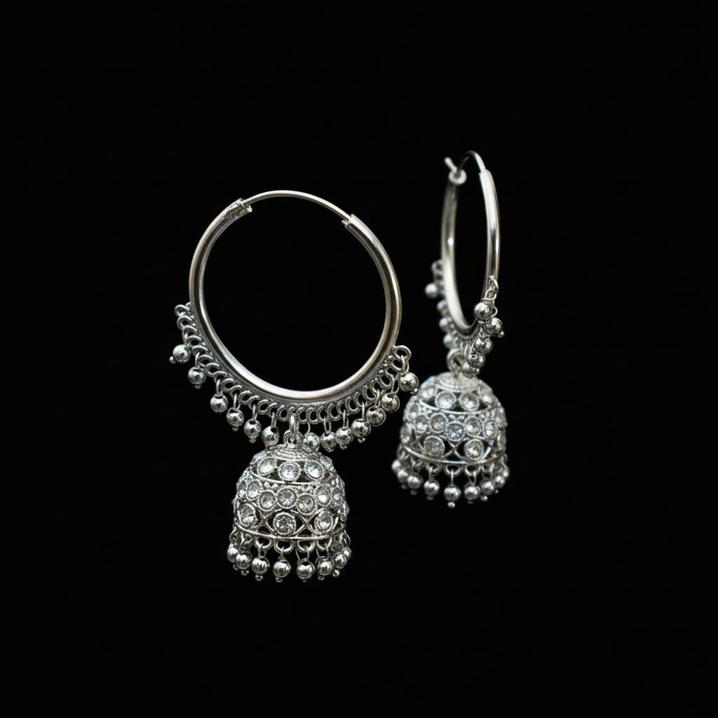 Silver hoop earrings with jhumka designs on a black stand against a dark background