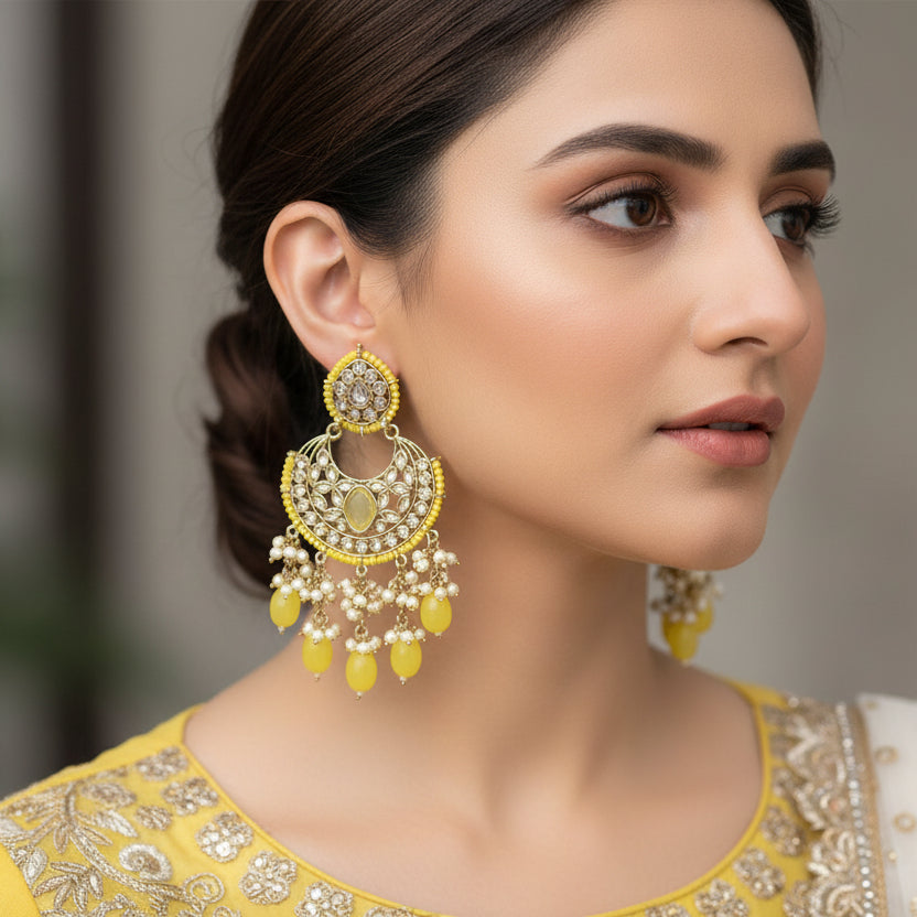 Pair of yellow and gold earrings with pearl-like beads on a dark background, branded 'Saheli'.