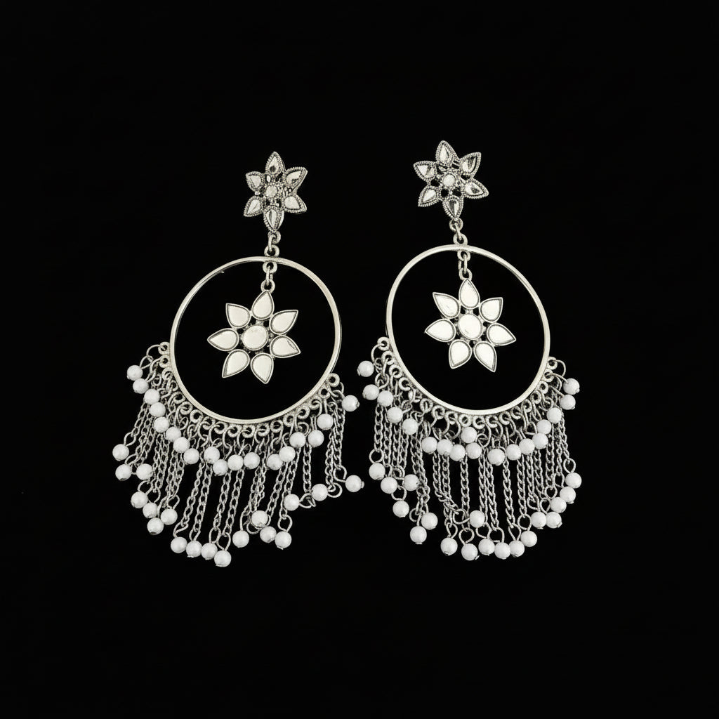 Pair of silver earrings with floral designs and dangling beads on a reflective surface.
