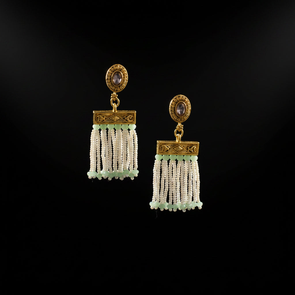 A pair of gold and white beaded dangle earrings displayed on a black jewelry stand against a dark gray background.