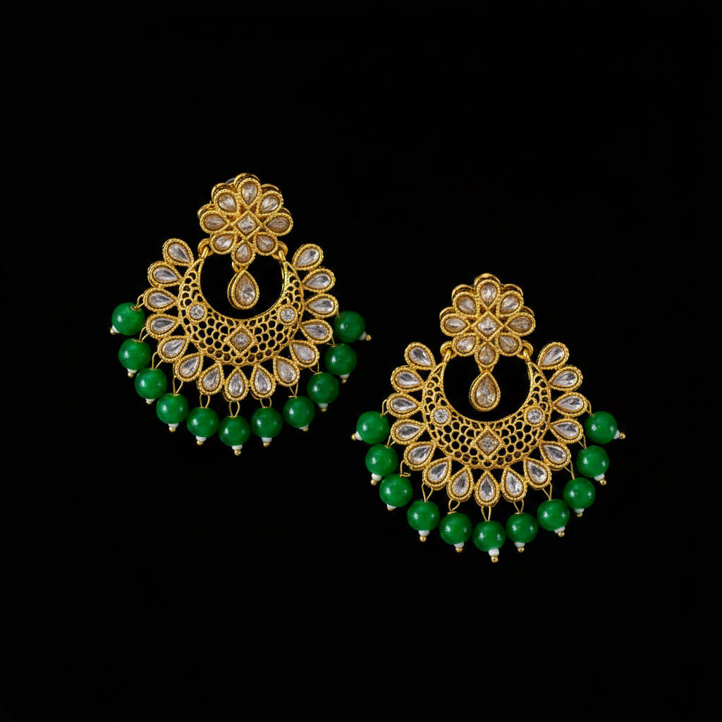 A pair of gold-plated Indian chandbali earrings with green bead fringe and clear stone accents, displayed on a dark gray reflective surface. A brand tag and 'SAHELL JEWELLERY' logo are visible.