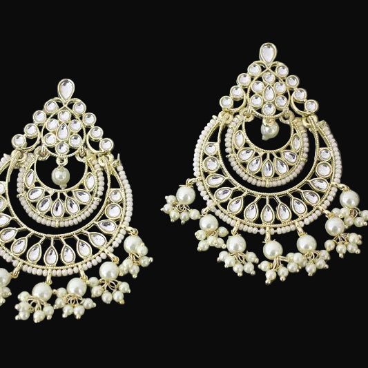 Ornate earrings with pearl-like stones on a dark background, featuring the brand 'Saheli'.