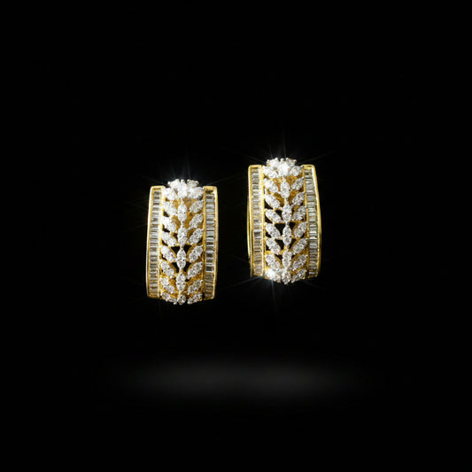 A pair of gold hoop earrings adorned with pavé-set clear stones and channel-set side stones, displayed on a dark reflective surface with the brand logo 'SAHELI MY BEST FRIEND' above them.