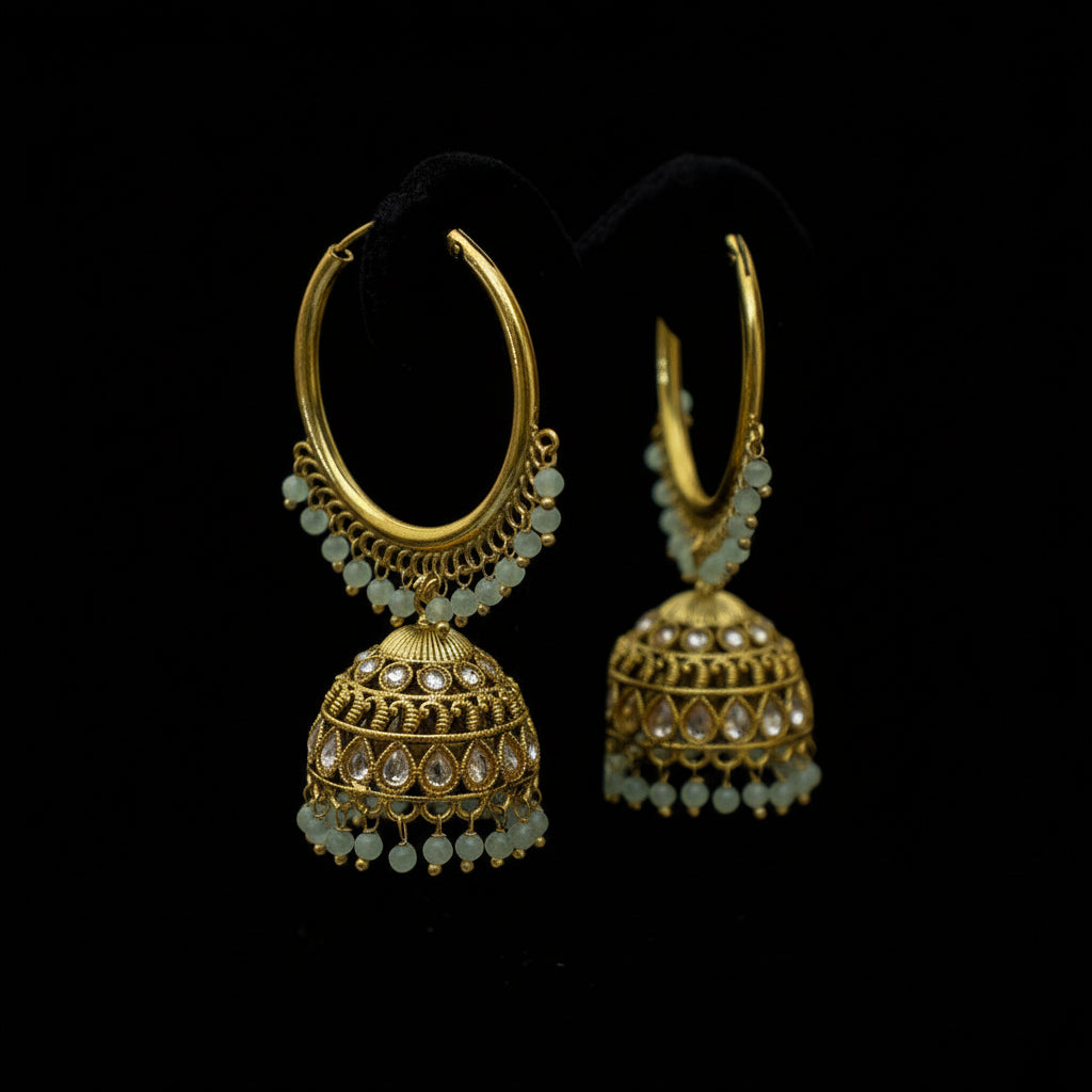 Gold hoop earrings with green beads on a black stand against a gray background