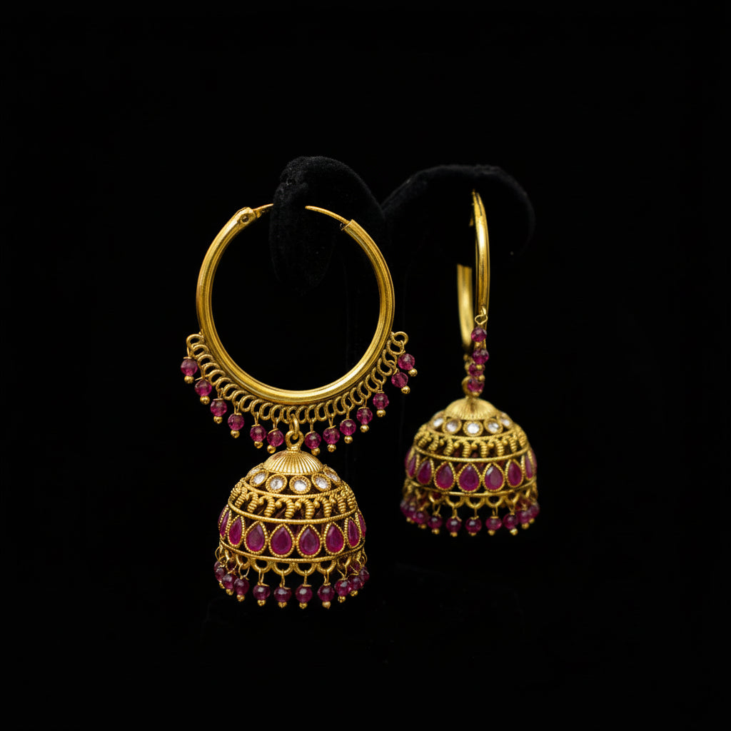 Gold and ruby earrings on a black stand with 'Saheli' branding.