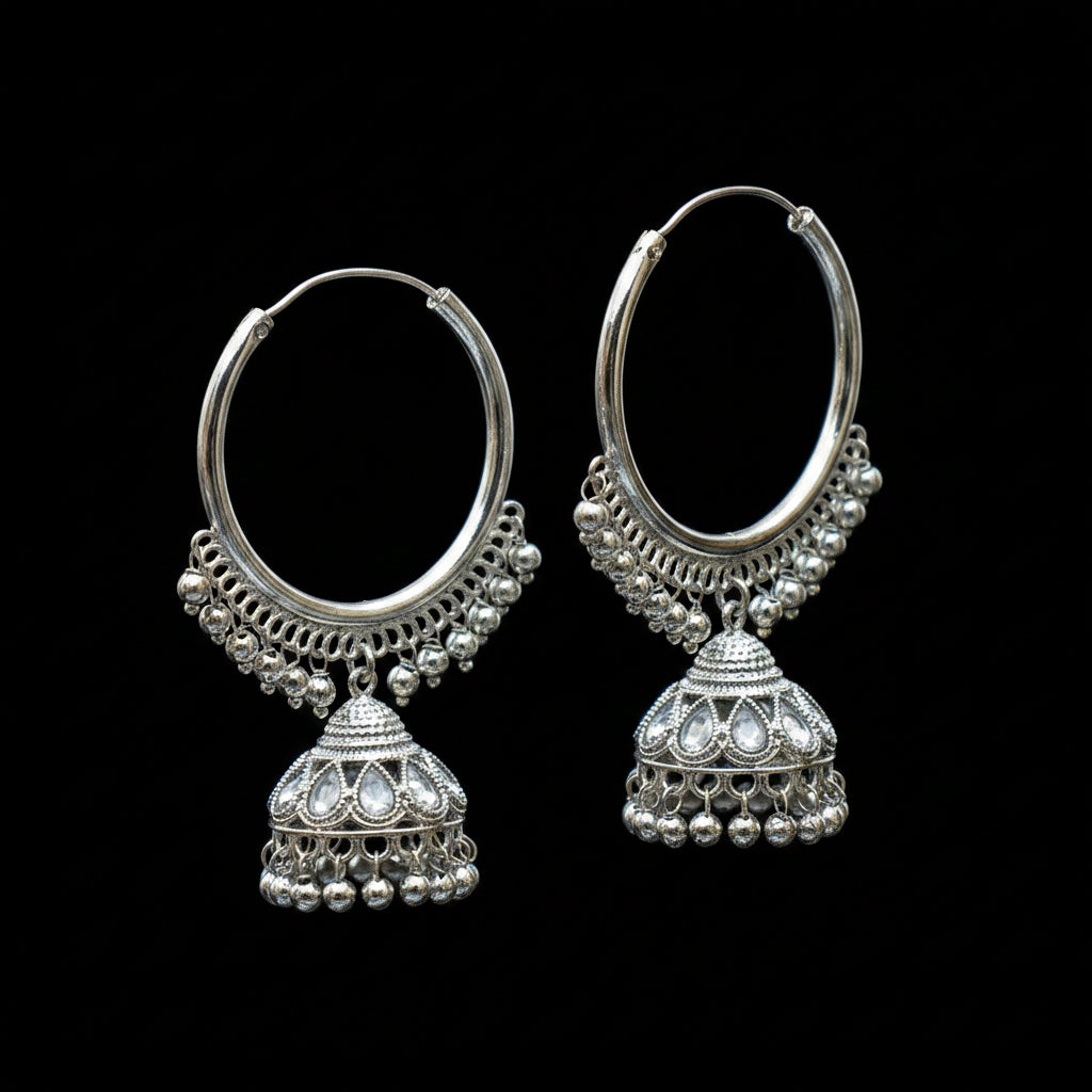 Silver hoop earrings with Jhumka designs on a black stand against a dark background.